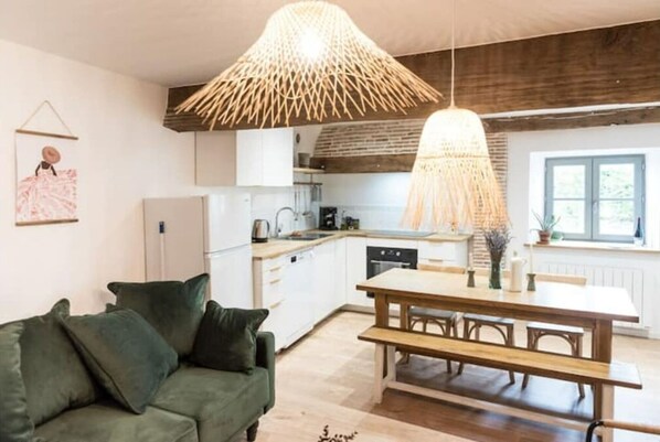 A modern kitchen with white cabinets, a wooden dining table, and a hanging light fixture.