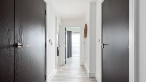 A hallway with dark wooden doors, light wooden flooring, and a view to a balcony with a window.