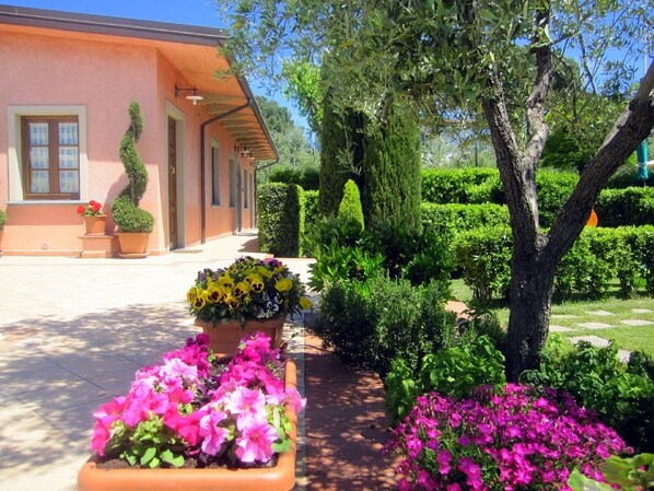 Un jardin bien entretenu, avec différents parterres de fleurs et des haies soigneusement taillées, devant un bâtiment à la façade rose.