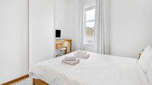 A hotel room with a large bed, a desk with a computer, and a window with curtains. - Charming and Spacious Apartment in Central Brixton - Pass the Keys (London)
