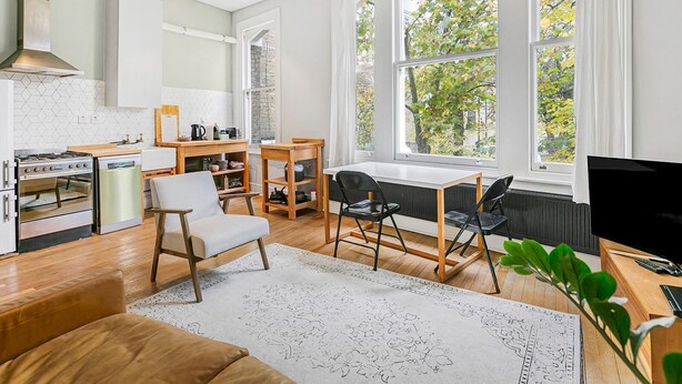 A modern kitchen with white cabinets, a stove, and a large window with a view of trees. - Charming and Spacious Apartment in Central Brixton - Pass the Keys (London)