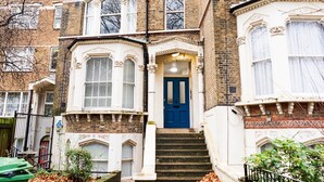 A multi-story brick building with a central entrance featuring a blue door, white-framed windows, and a small porch area. - Charming and Spacious Apartment in Central Brixton - Pass the Keys (London)