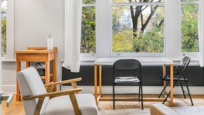 A modern living room with a large window, a wooden table, a grey armchair, and a black folding chair. - Charming and Spacious Apartment in Central Brixton - Pass the Keys (London)