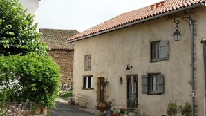 A narrow street with traditional stone buildings, wooden shutters, and potted plants.
