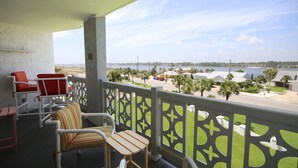 A balcony with a view of the beach, a table, and two chairs.