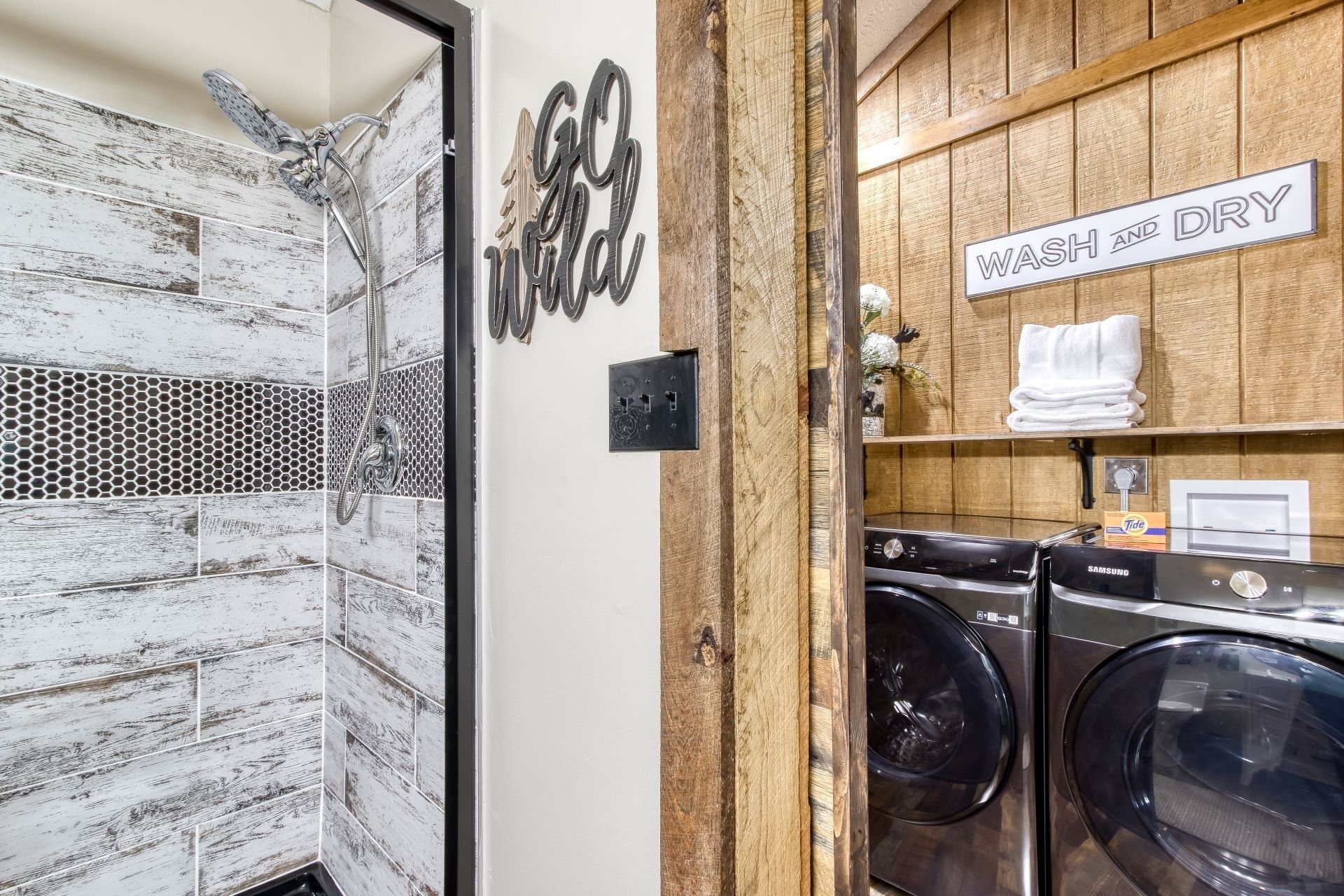 A bathroom with a shower, a sign that says "Welcome," and a sign that says "Wash and Dry." There are two washing machines and a towel rack with towels.
