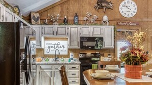 Una cocina con armarios de madera, un refrigerador, un microondas y un reloj en la pared.