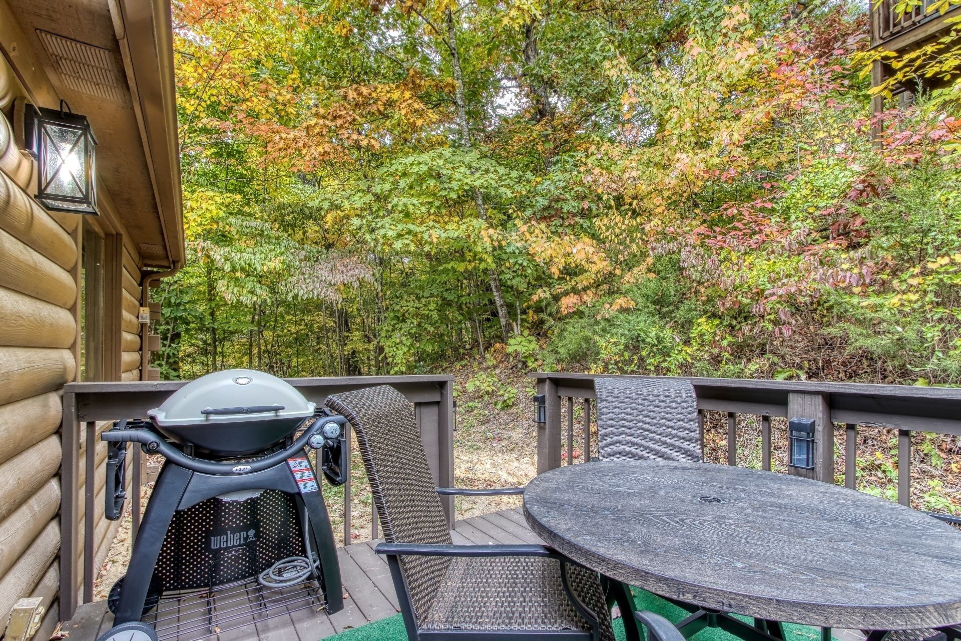 A wooden deck with a grill, wicker chairs, and a table.