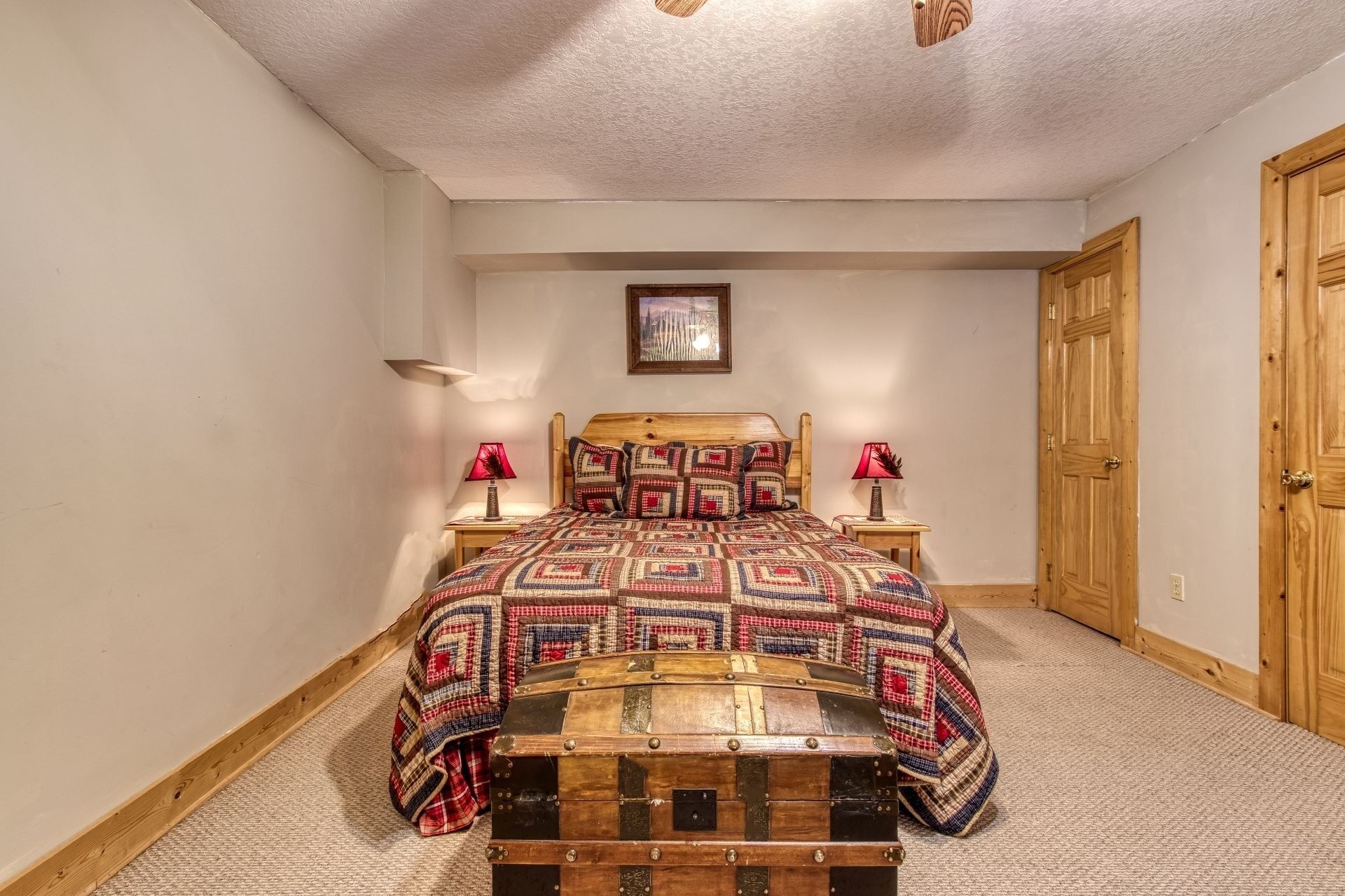 Quarto com cama de madeira, duas luminárias de cabeceira, porta de madeira e um quadro na parede.