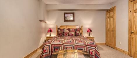 Quarto com cama de madeira, duas luminárias de cabeceira, porta de madeira e um quadro na parede.