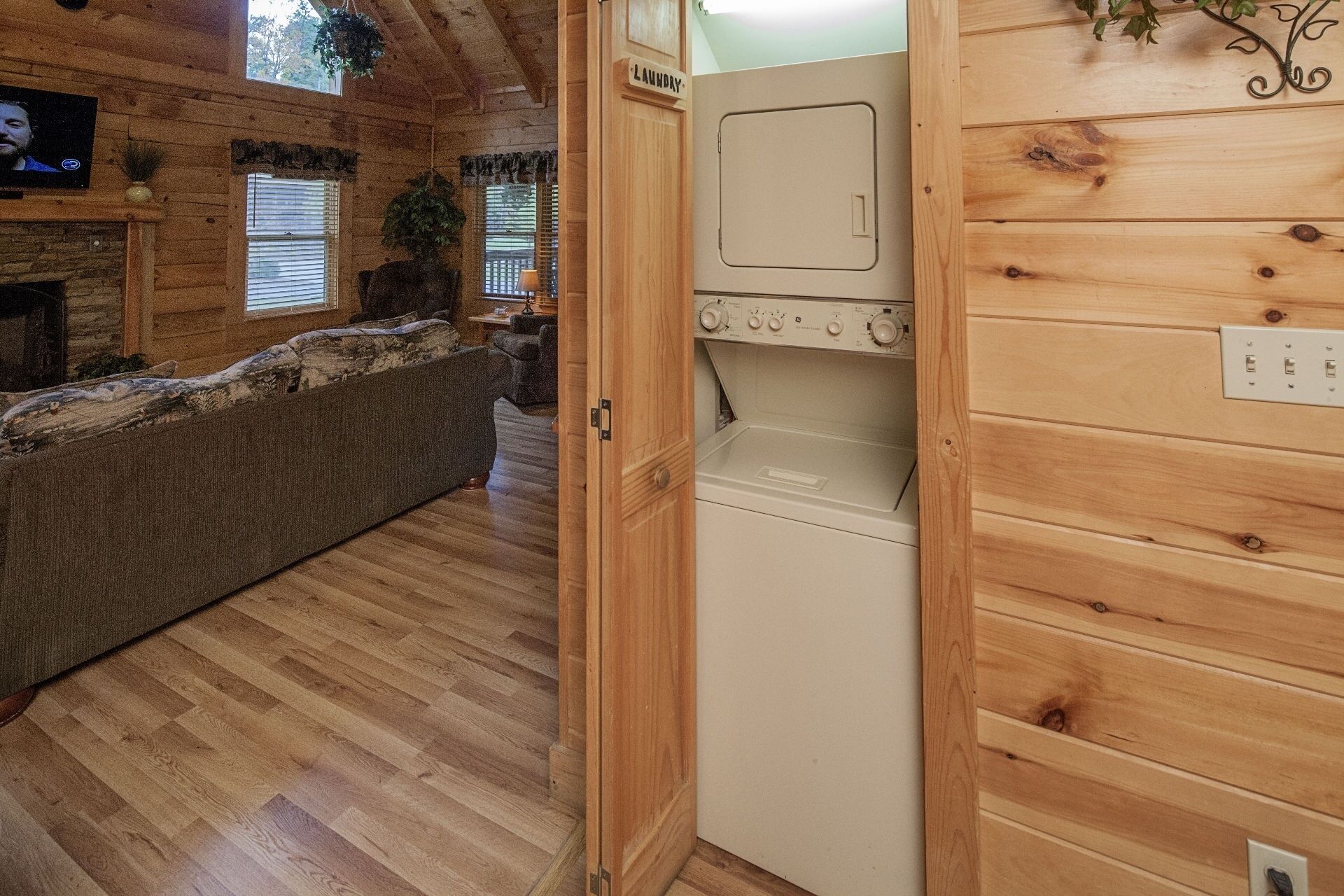 Interior acogedor de una cabaña con piso de madera, un sofá, televisor y un área de lavandería con lavadora.