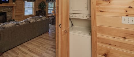 Interior acogedor de una cabaña con piso de madera, un sofá, televisor y un área de lavandería con lavadora.
