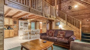 A spacious living area with a wooden staircase, a dining table with chairs, and a leather sofa. - Er2 - Heavenly View Great Location! - Close To Town! 2 Bedroom Cabin by RedAwning (Pigeon Forge)