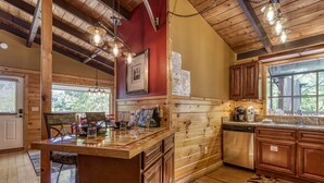 A rustic cabin interior with a wooden dining area, kitchen with wooden cabinets, and a large window. - Gatlinburg Views A Unique Cabin Mountain Views Expansive Decks Adjacent To Gatlinburg & Ski Lodge 1 Bedroom Cabin by RedAwning (Gatlinburg)
