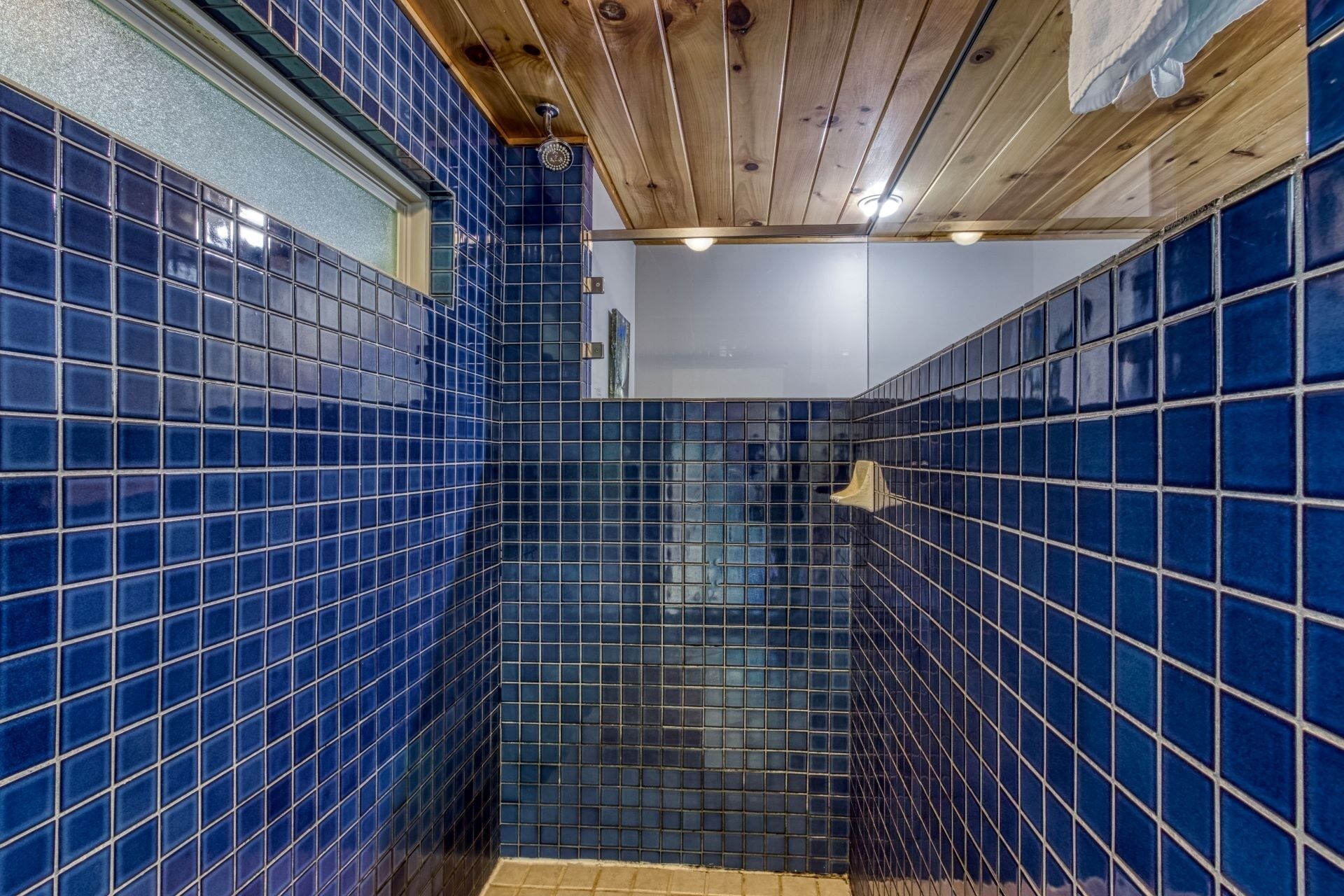 A bathroom with blue-tiled walls and a wooden ceiling.