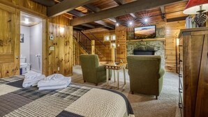 A wooden cabin interior with a bed, two green armchairs, a small table, and a fireplace. - Gatlinburg Views A Unique Cabin Mountain Views Expansive Decks Adjacent To Gatlinburg & Ski Lodge 1 Bedroom Cabin by RedAwning (Gatlinburg)