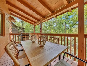 Une terrasse en bois avec une table et des chaises, un barbecue et une vue sur les arbres.