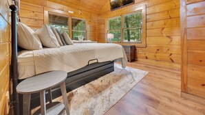 Une chambre dans une cabane en bois, avec un lit, une petite table, un ventilateur de plafond et un téléviseur fixé au mur.