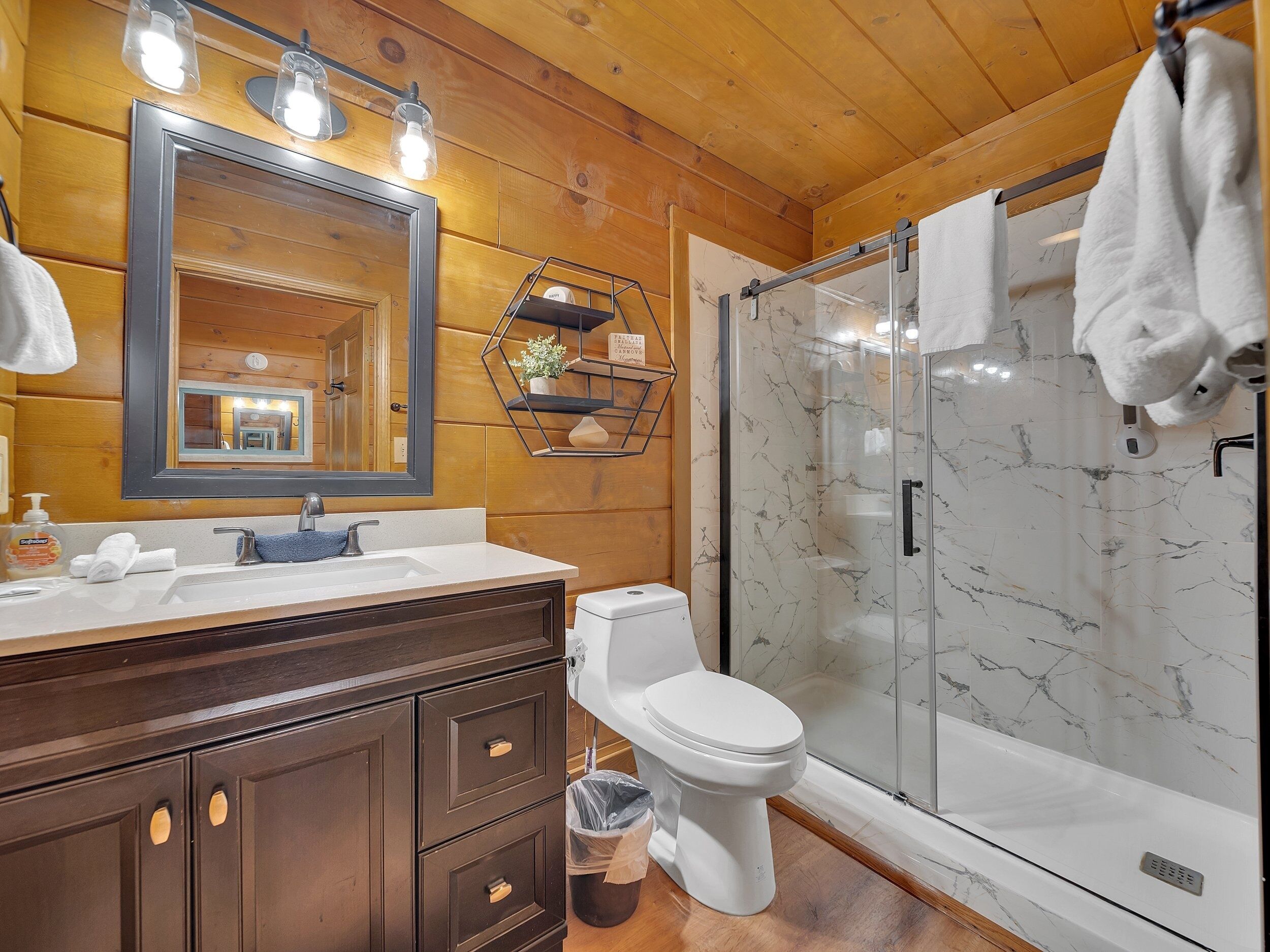 Un baño moderno con tocador de madera, un espejo grande, cabina de ducha de vidrio y pared de ducha con azulejos de mármol.