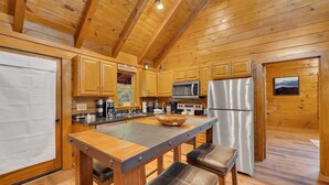 Une cuisine rustique, aménagée dans une cabane en bois, avec un îlot central, des appareils en acier inoxydable et un panneau d’accueil.