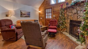 A cozy living room with a fireplace, wooden walls, and a Christmas tree. - Er46 - Cherith Brook - Great Location. Just Across From Swimming Pool! 2 Bedroom Cabin by RedAwning (Pigeon Forge)