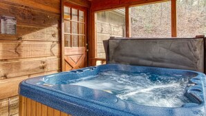 A wooden cabin with a hot tub in the center, large windows, and a door with a glass panel. - Er46 - Cherith Brook - Great Location. Just Across From Swimming Pool! 2 Bedroom Cabin by RedAwning (Pigeon Forge)