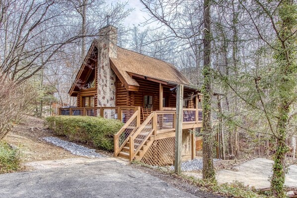 A log cabin with a stone chimney, wooden deck, and a staircase leading to the entrance.