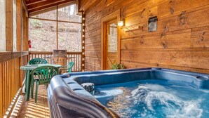 Una cabaña de madera con un jacuzzi, una parrilla y una mesa con sillas.