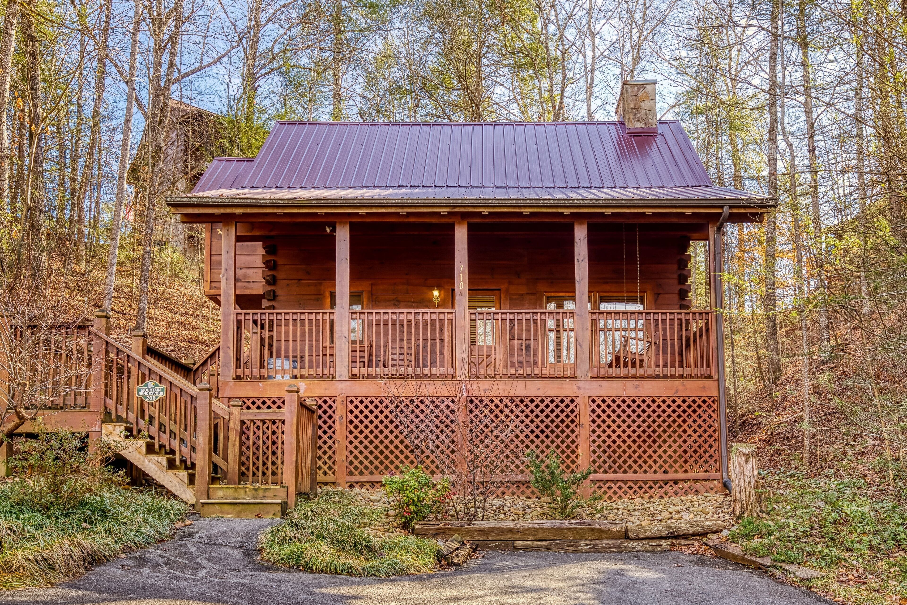 A rustic cabin with a wooden exterior, a metal roof, and a covered porch with a lattice railing.