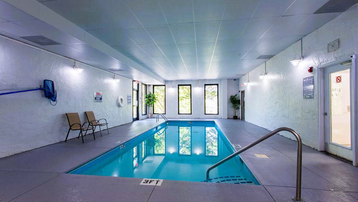 An indoor swimming pool with a 3ft depth marker, chairs, and a door with a sign.