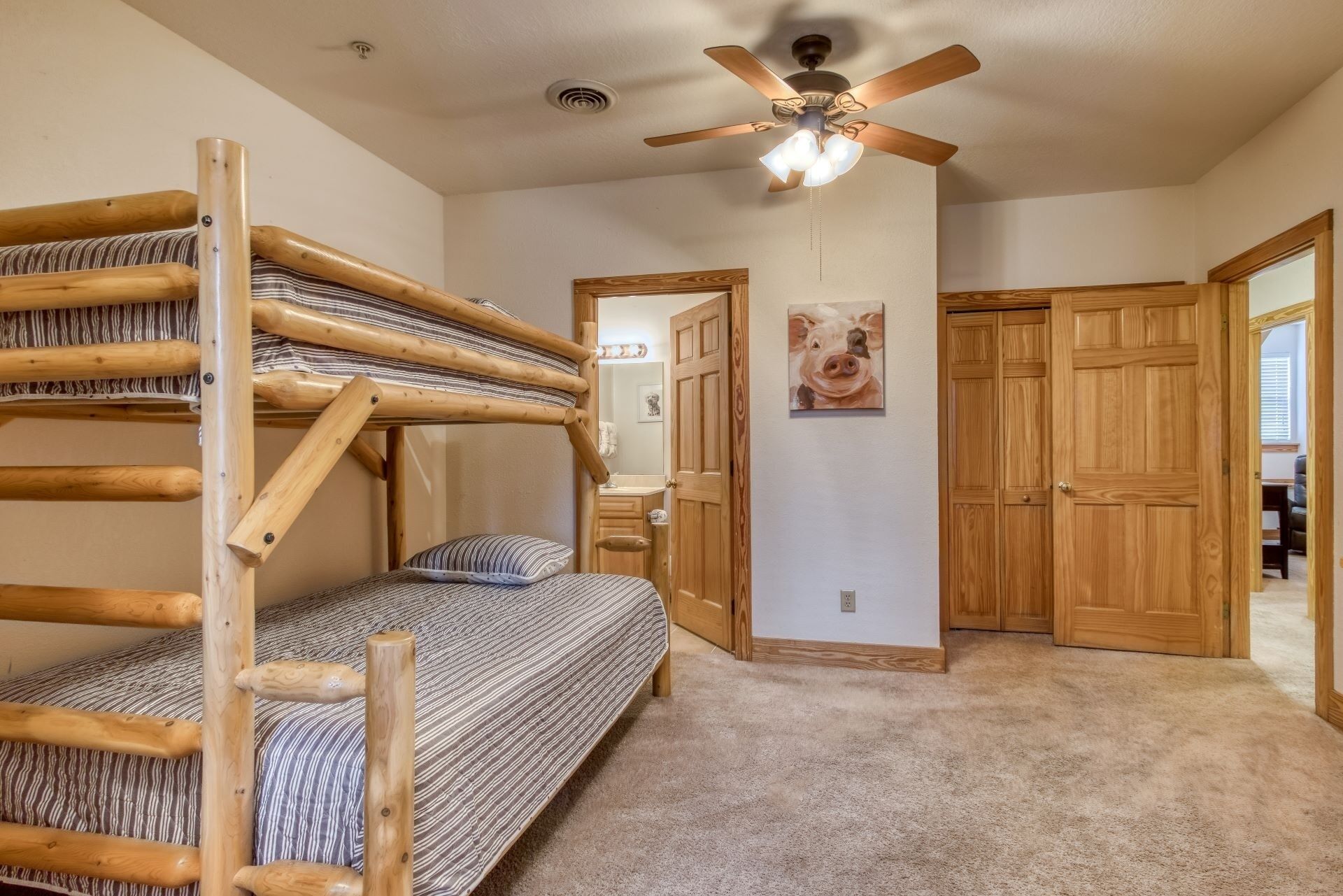 A room with bunk beds, a ceiling fan, wooden doors, and a painting on the wall.