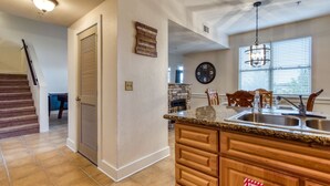 A kitchen with a stone fireplace, wooden cabinets, a granite countertop, and a large clock on the wall. - Owl See You 3205 - Close To Dollywood And Overlooking Gatlinburg Golf Course 2 Bedroom Condo by RedAwning (Pigeon Forge)