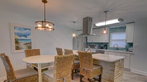 A modern kitchen with a central island, white cabinetry, and a dining area with wicker chairs.