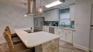 A modern kitchen with white cabinetry, a central island, stainless steel appliances, and a hanging light fixture.