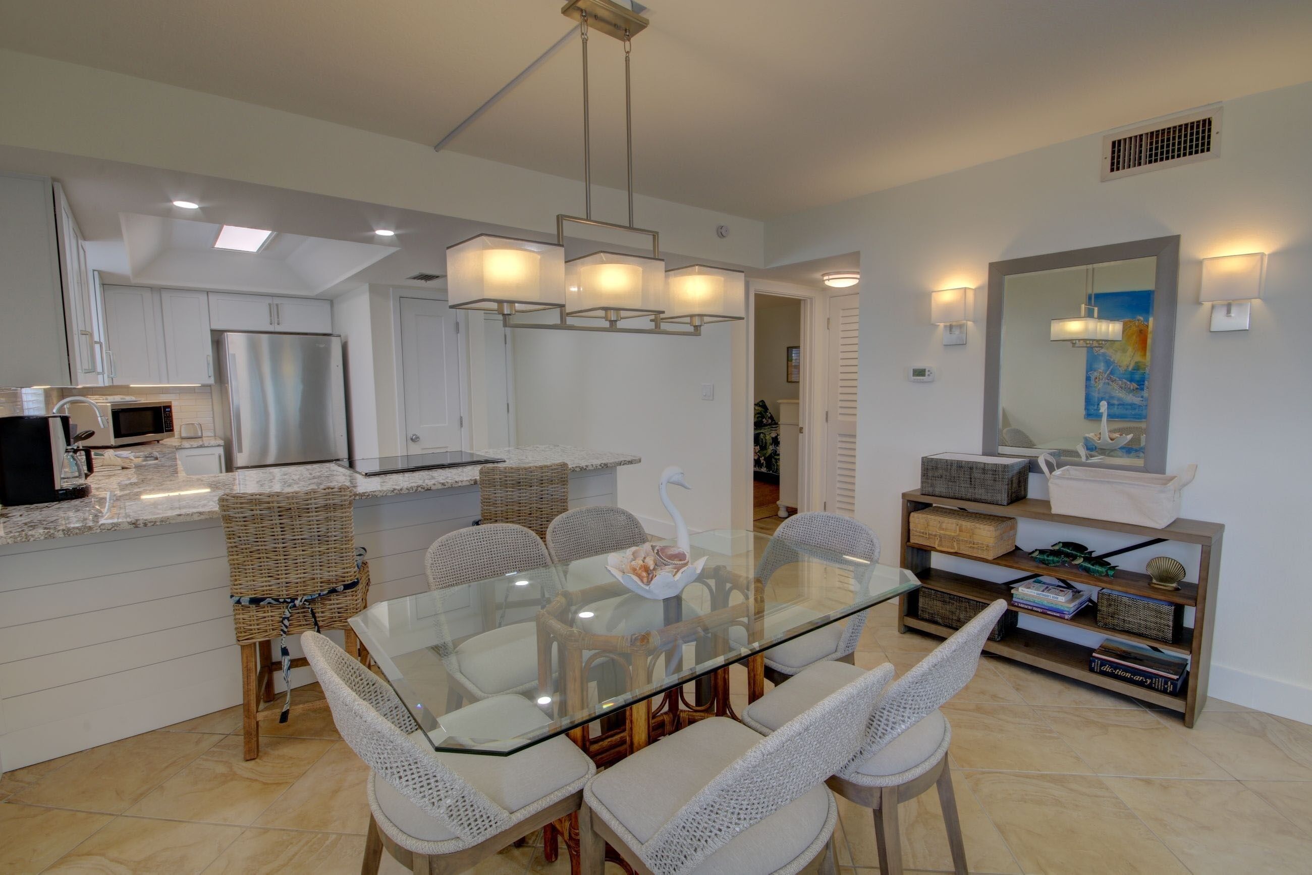 Una cocina moderna con armarios blancos, un refrigerador de acero inoxidable y una mesa de comedor de vidrio con sillas de mimbre.