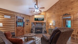 A log cabin interior with a fireplace, leather furniture, and a 'welcome' sign.