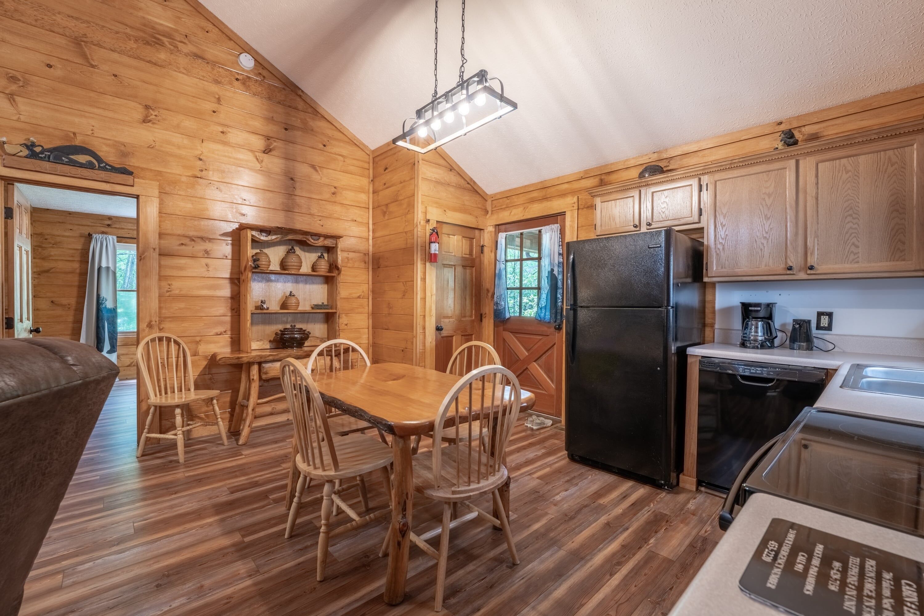 L’intérieur d’un chalet en bois comprend une table à manger, des chaises, un réfrigérateur noir, une machine à café et des placards en bois.