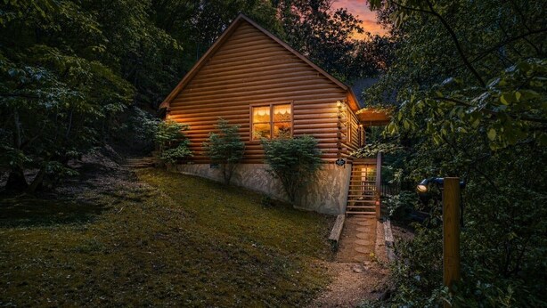 A log cabin with a wooden exterior, a front porch, and a staircase leading to the entrance.