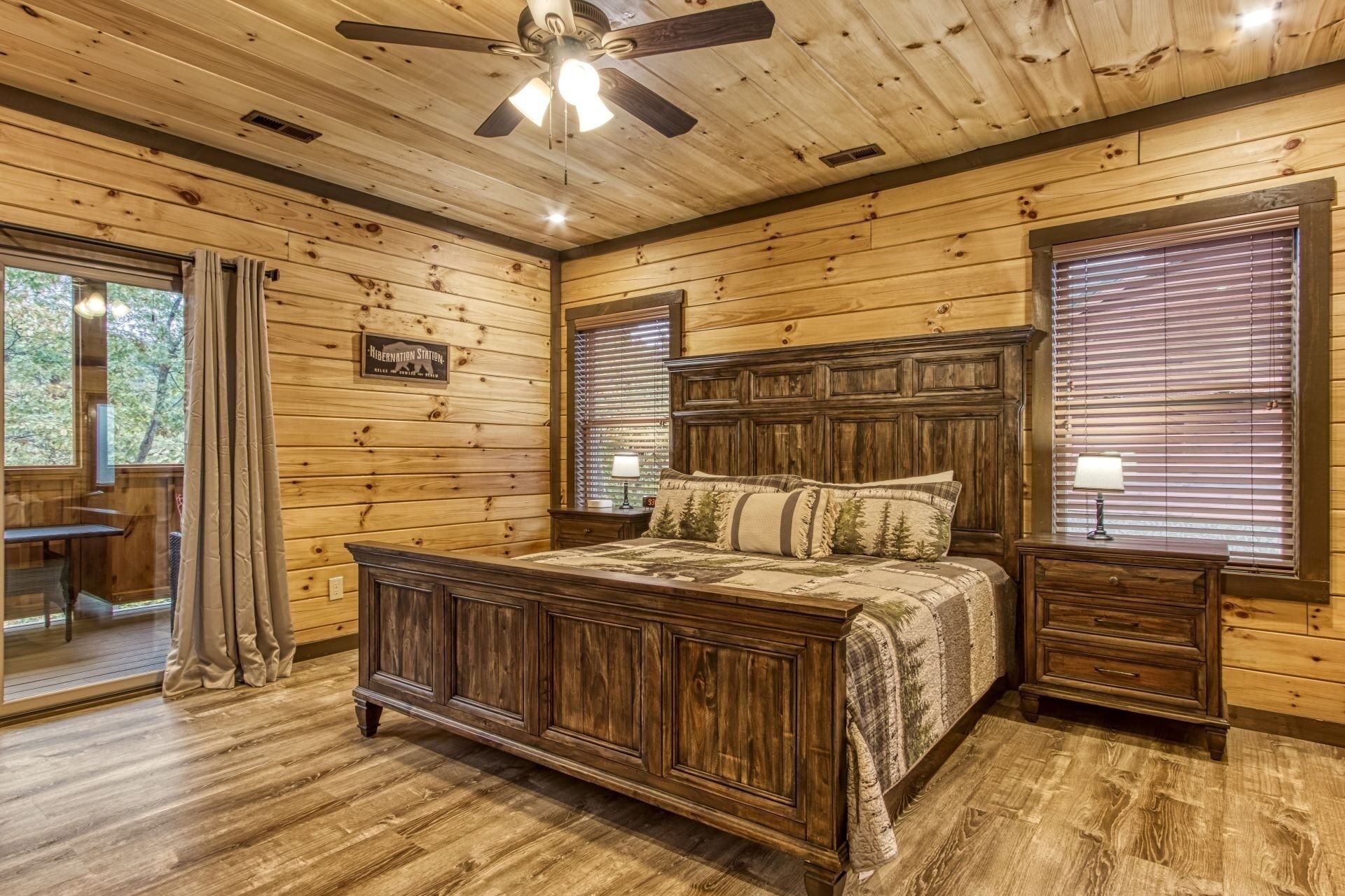 A wooden cabin bedroom with a bed, nightstands, a ceiling fan, and a window with blinds.