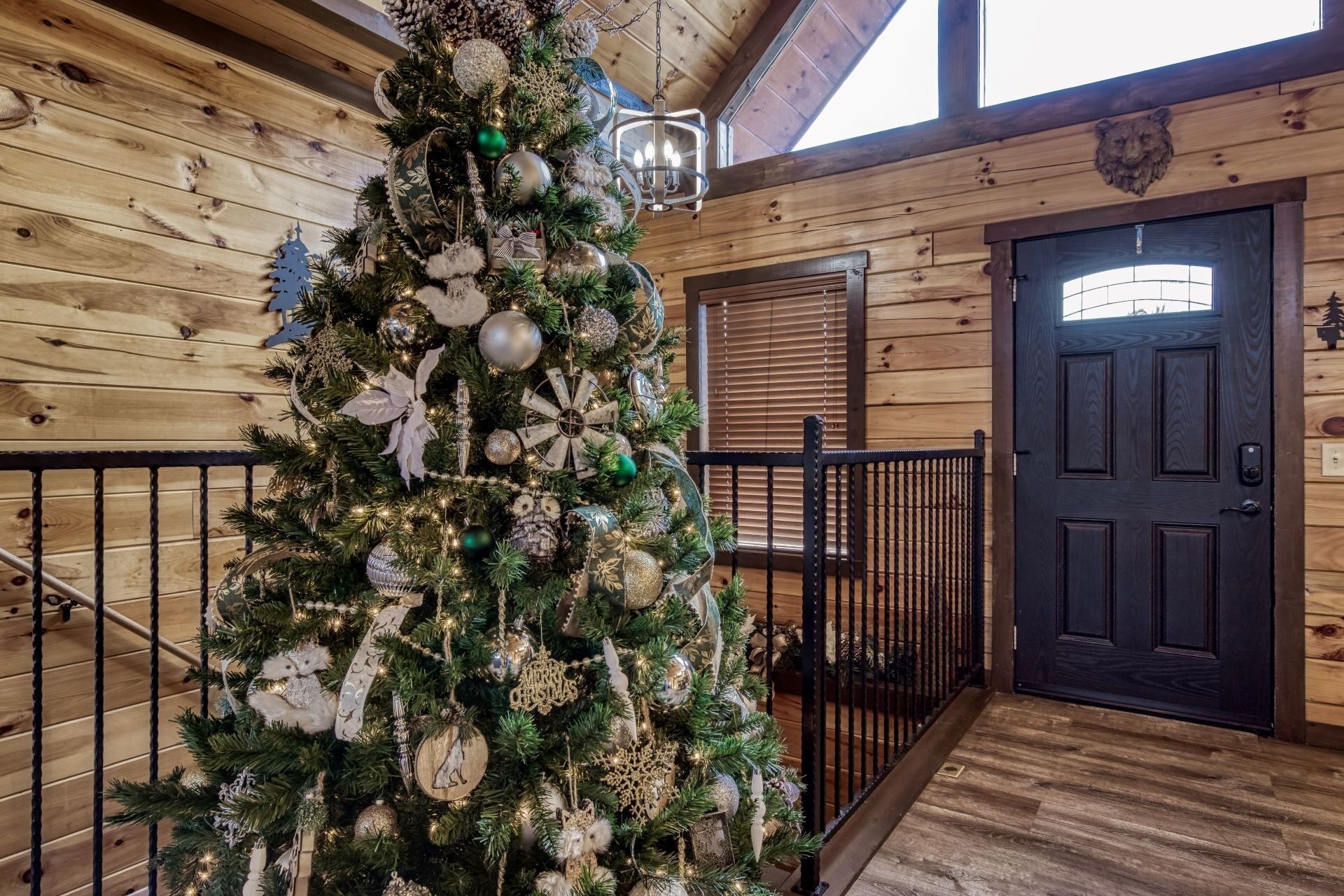 Un sapin de Noël dans un intérieur en bois, avec une porte noire et une fenêtre équipée de stores.