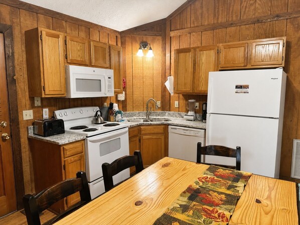 Una cocina con armarios de madera, microondas, estufa, refrigerador, pileta y una mesa con sillas.