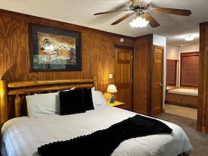 Ein Schlafzimmer mit Holzwänden, einem Bett, einem Deckenventilator, einem Gemälde und einer Badezimmertür.