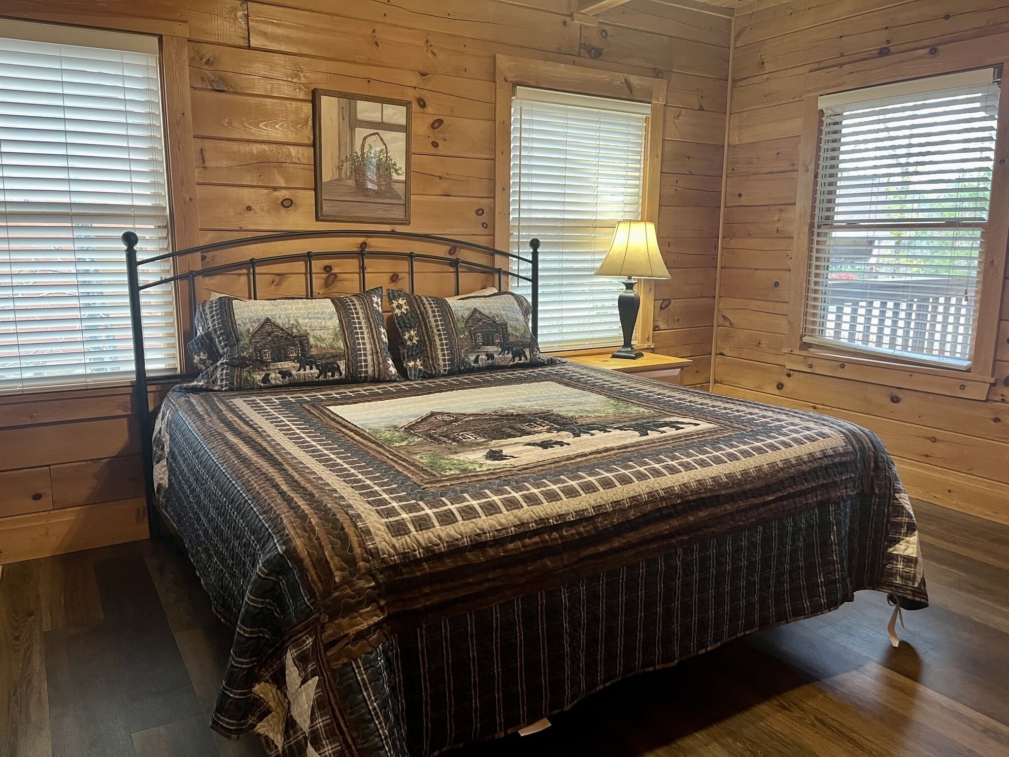 A wooden-paneled bedroom with a bed, pillows, a bedside lamp, and a framed picture on the wall.