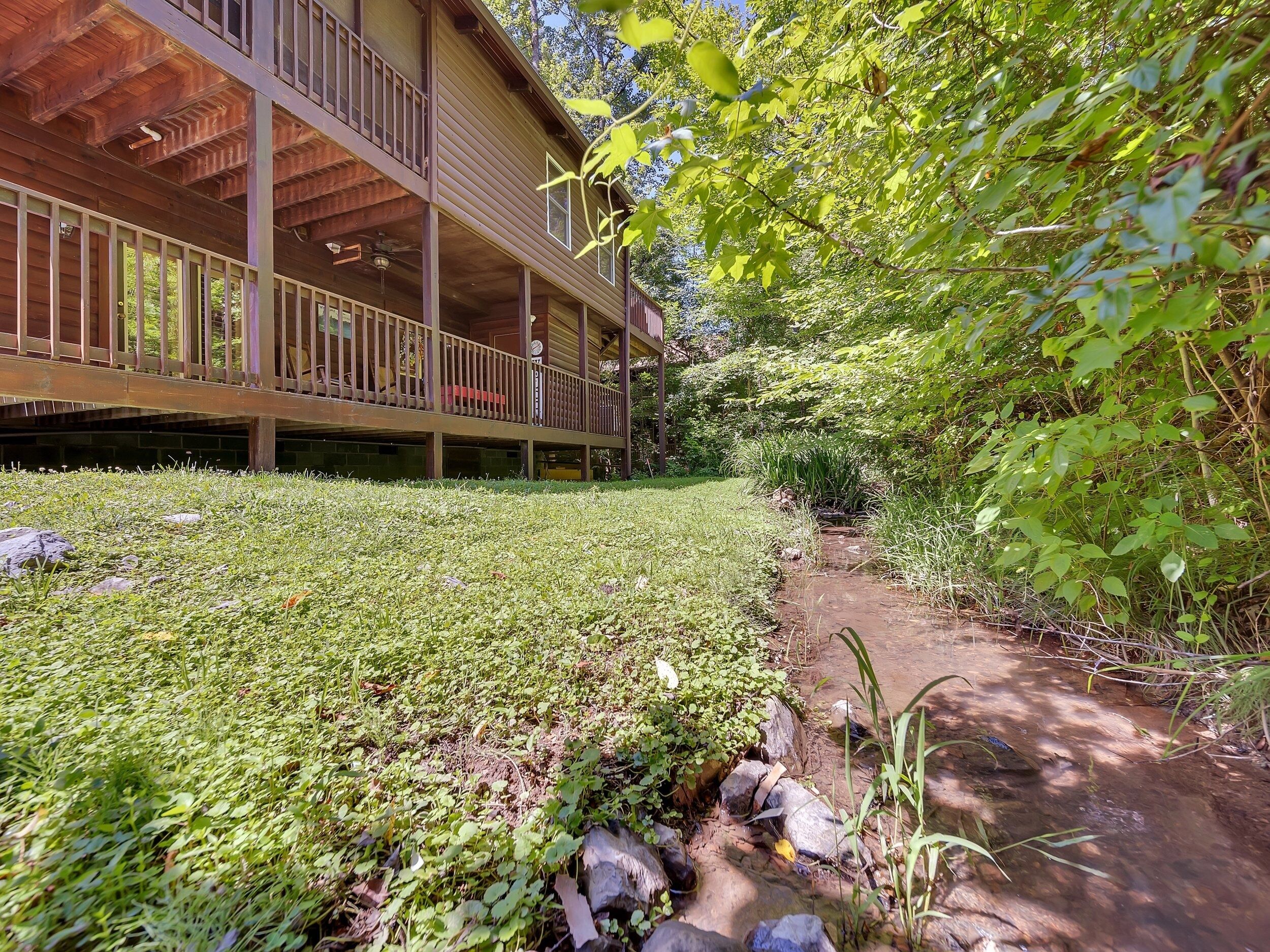 A wooden building with a covered porch and a small stream running alongside.