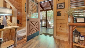 A wooden cabin interior with a large wooden door, a small table with a lamp, and a wooden bench with a sign. - Er258- Sweet Memories Great Location- Close To Town 5 Bedroom Cabin by RedAwning (Pigeon Forge)