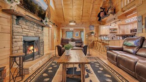 A cozy log cabin interior with a stone fireplace, leather furniture, and a kitchen area. - Er258- Sweet Memories Great Location- Close To Town 5 Bedroom Cabin by RedAwning (Pigeon Forge)