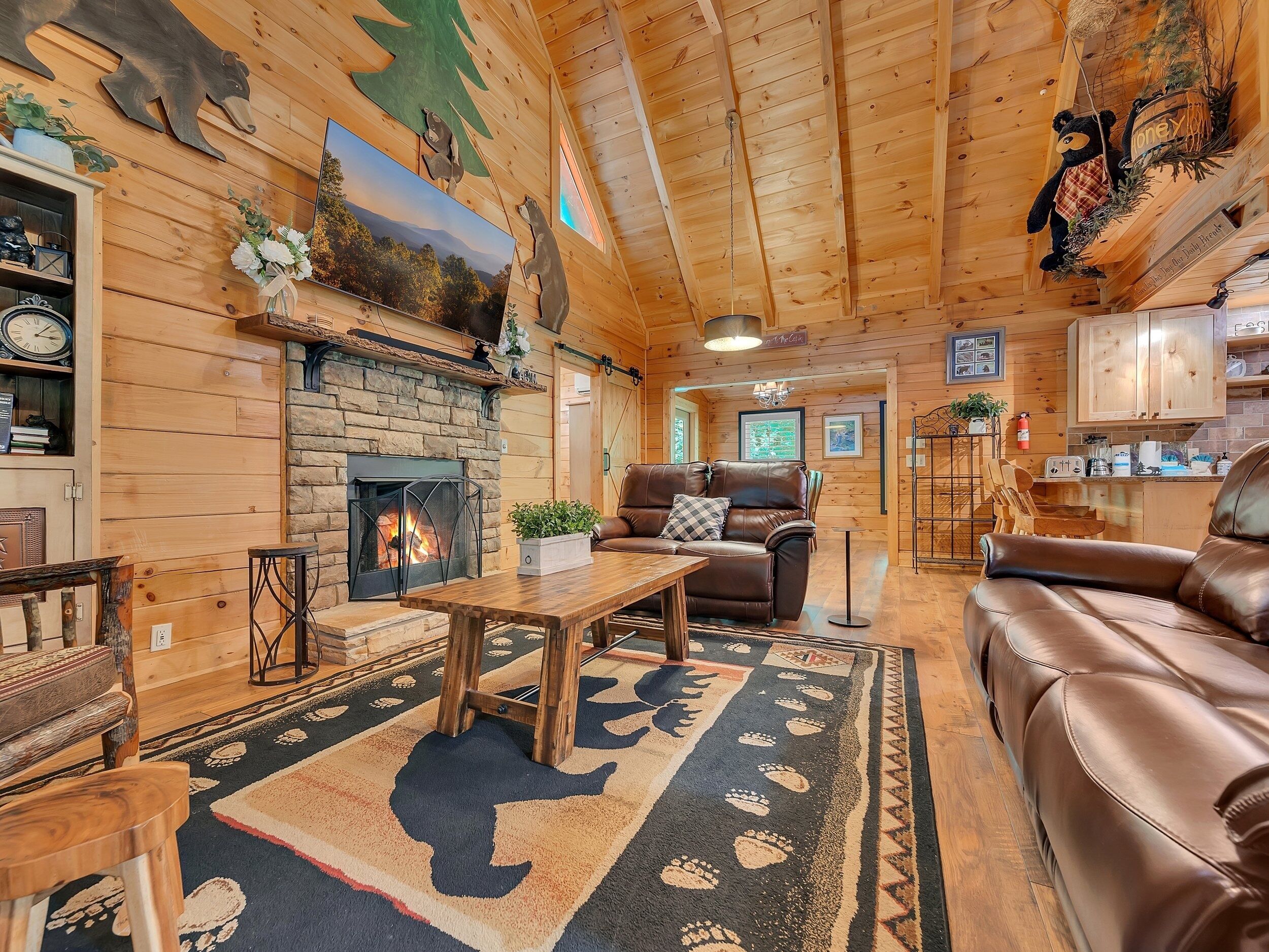 A cozy cabin interior with a fireplace, leather furniture, wooden walls, and a bear-themed decor.