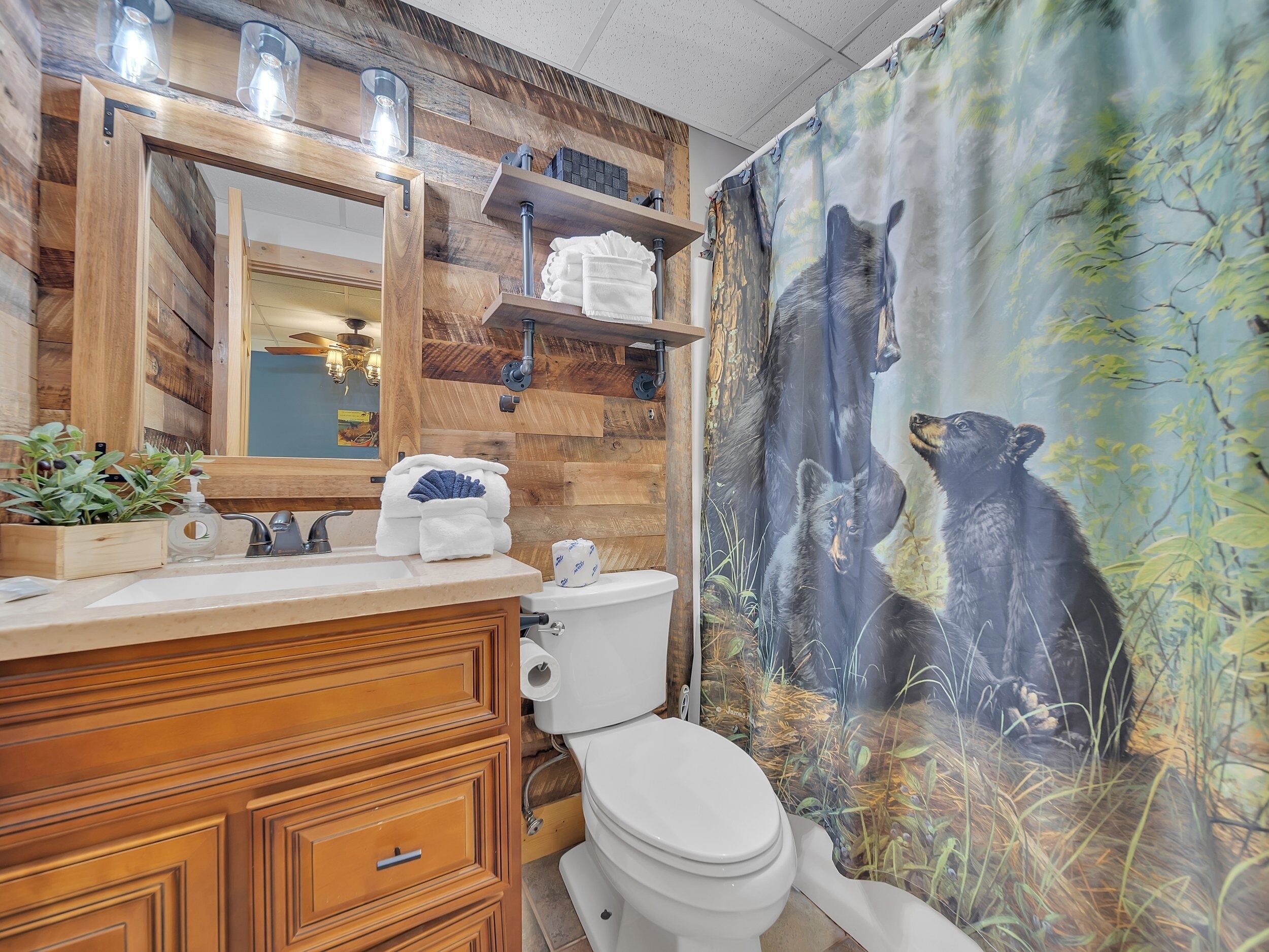 A bathroom with a wooden vanity, a mirror, a sink, and a toilet. There is a bear-themed shower curtain.