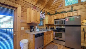 A wooden cabin kitchen with a refrigerator, microwave, oven, and dishwasher. - ER244 - Black Hawk Hideaway Great Location - Close To Town! 2 Bedroom Cabin by RedAwning (Pigeon Forge)
