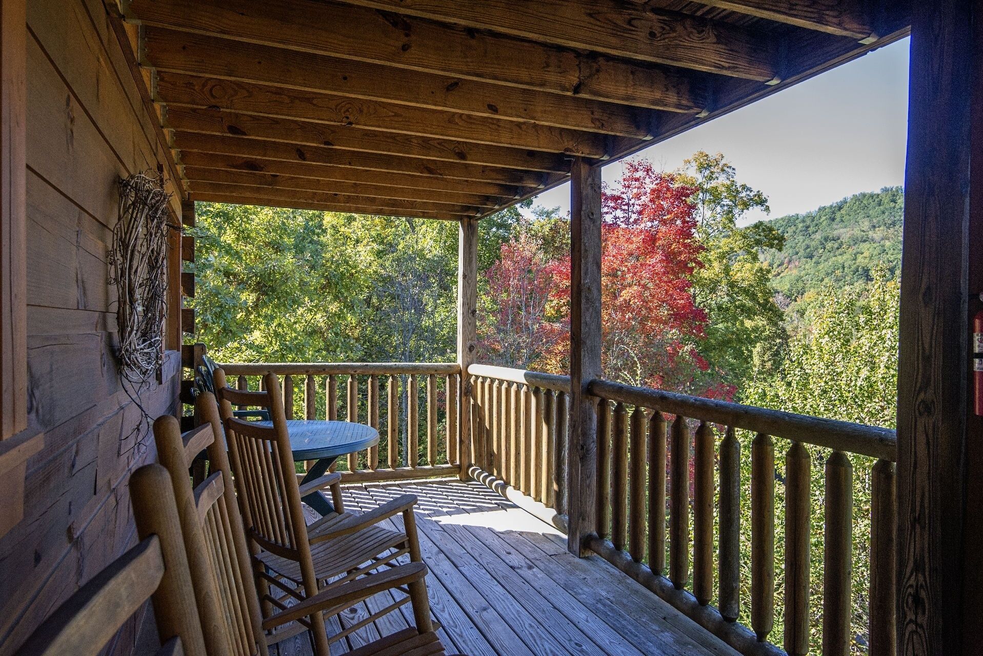 A wooden deck with a table and chairs, overlooking a forested area with autumn foliage.